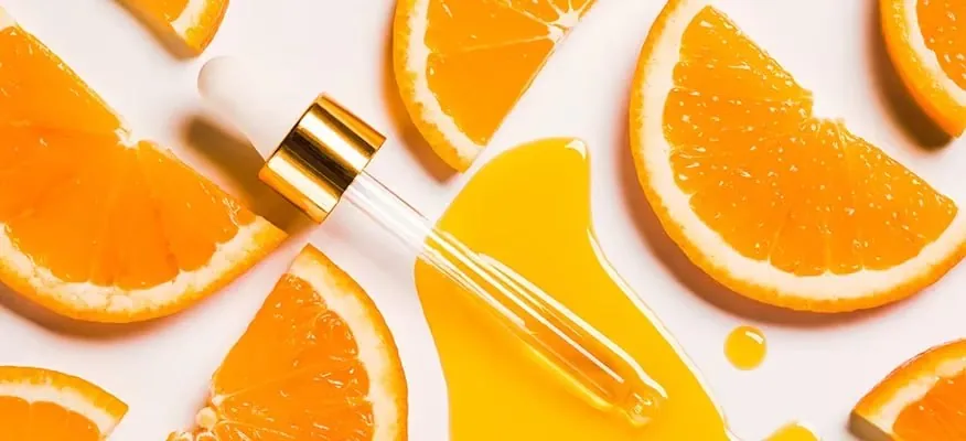 Vitamin C serum dropper surrounded by fresh orange slices